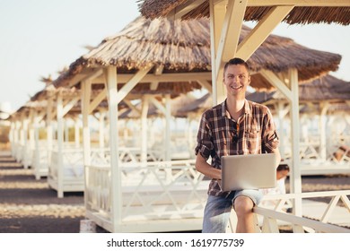 Happy young student guy working with a laptop while sitting under a straw canopy on a warm summer morning. The concept of studying and preparing for summer exams - Shutterstock ID 1619775739