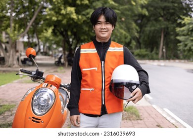 Happy young Thai motorcycle taxi driver or rider waiting for passenger near by the building in the city.