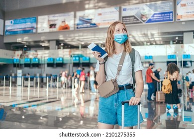 Happy Young Tourist Woman In A Protective Medical Mask Holding Passport At International Airport. Travel After Covid-19 Pandemic