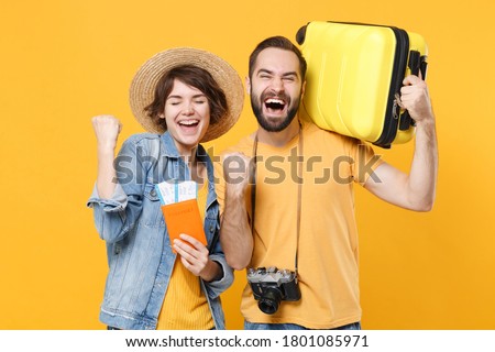 Happy young tourists couple friends man woman isolated on yellow background. Passenger traveling abroad on weekends. Air flight journey concept. Hold passport tickets suitcase doing winner gesture