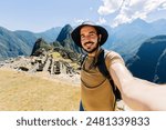 Happy young traveler man taking selfie portrait while enjoying vacation in Peru. Joyful tourist visiting Machu Picchu. Travel and holiday lifestyle concept.
