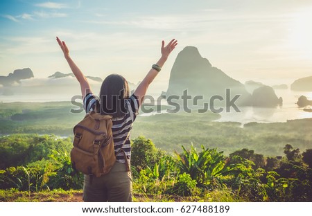 Happy young traveler woman backpacker raised arm up to sky enjoying a beautiful of nature at top of mountain and sea view,Freedom wanderlust concept