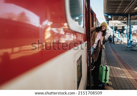 Happy young traveler woman with luggage getting off the train at train station platform
