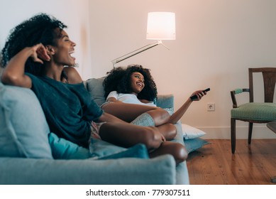 Happy young two black women lying down in the couch watching tv  