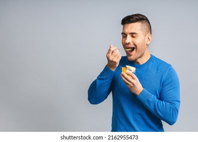 Happy Young Ukrainian Handsome Man Eating Yogurt Isolated Over Grey White Background. Healthy Lifestyle Concept.