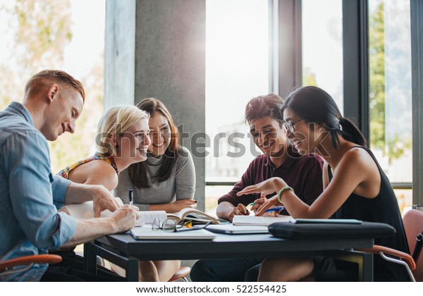 Happy young university students studying with books in library. Group of multiracial people in college library.