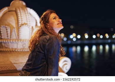 Happy Young Urban Woman Looking Up To Sky At Night On Bridge, Budapest, Hungary