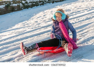 Happy Young Vibrantly Dressed Girl Sledging With Blue Ear Muffs