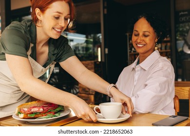 Happy young waitress serving a customer a sandwich and a cup of coffee in a modern cafe. Cheerful young woman working in a fast food restaurant. - Powered by Shutterstock