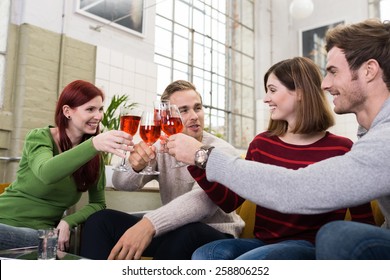 Happy Young White Friends in Casual Long Sleeve T-Shirts Tossing a Glass of Drink While Resting at Living Room - Powered by Shutterstock