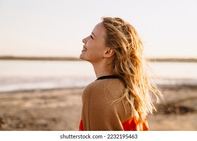 Happy young white woman smiling while walking by seashore on sunny day - Powered by Shutterstock