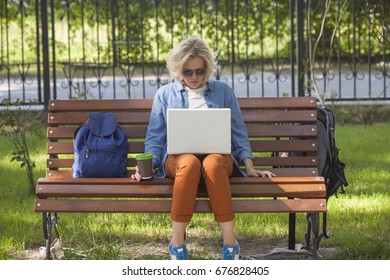 Happy Young Woman Admires Something Beautiful, Sitting With An Open Net-book Kneeling In The Park, Charming Woman With A Smile, Thinking Of A Wonderful Trip While Working On A Laptop Computer Outside