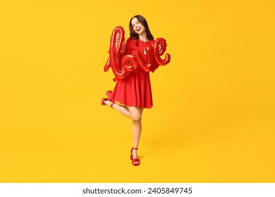 Happy young woman with air balloons in shape of word LOVE on yellow background. Valentine's Day celebration