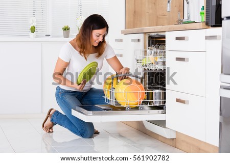 Happy Young Woman Arranging Plates In Dishwasher At Home