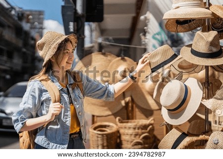 Happy young woman asian is visit local market during her trip and purchase straw hat handmade. Tourist women travel enjoy shopping market during holidays, backpacker traveller
