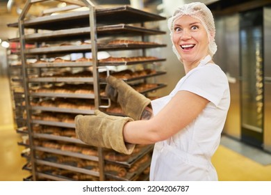 Happy Young Woman Baker Apprentice Pushing Shelf Trolley With Fresh Baked Goods In Bakery