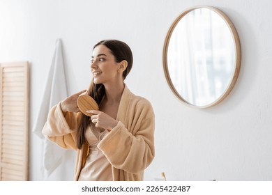 happy young woman in bathrobe brushing hair in white modern bathroom - Powered by Shutterstock