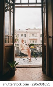 Happy Young Woman In Bathrobe Enjoying Food And Drink While Relaxing On The Balcony