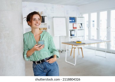Happy young woman with a beaming vivacious smile leaning against an internal pillar in a spacious high key office looking to the side with copyspace - Shutterstock ID 2118804326