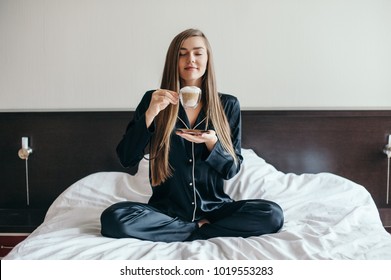 Happy young woman in bed with cup of coffee in hands