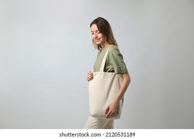 Happy young woman with blank eco friendly bag on light background - Powered by Shutterstock