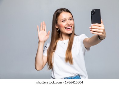 Happy young woman blogger influencer holding modern smart phone wave hand hello. Smiling vlogger girl looking at mobile make video call, shooting vlog taking selfie on grey background - Powered by Shutterstock