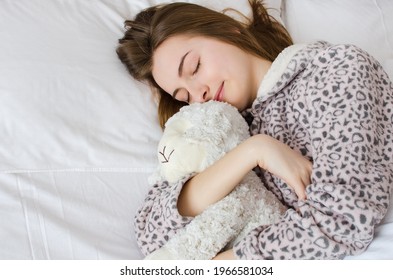 Happy Young Woman With Blonde Hair Sleeping In An Embrace With A Stuffed Animal Toy. Favorite Sheep In The Hands Of Teen Girl In Cute Warm Pajamas Close-up And Space On The Left. Top View. Copy Space.