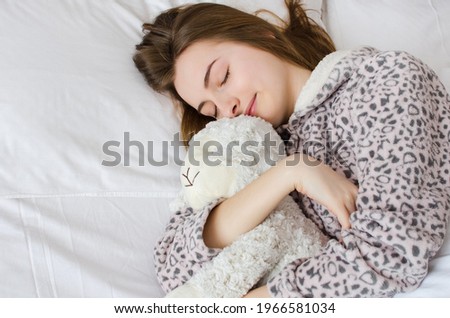 Happy young woman with blonde hair sleeping in an embrace with a stuffed animal toy. Favorite sheep in the hands of teen girl in cute warm pajamas close-up and space on the left. Top view. Copy space.