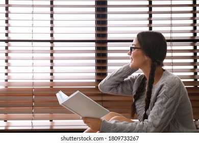 Happy young woman with book near window at home. Lazy morning - Shutterstock ID 1809733267