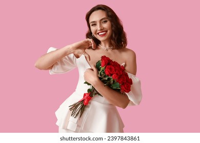 Happy young woman with bouquet of red roses on pink background