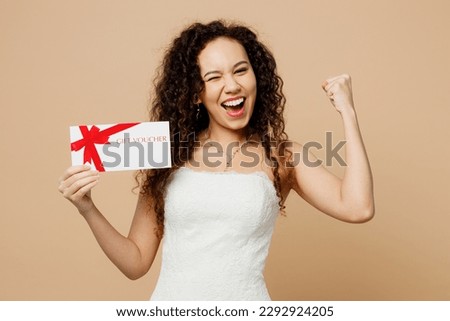 Happy young woman bride in wedding dress posing hold store gift certificate coupon voucher card do winner gesture isolated on plain beige background studio portrait. Ceremony celebration party concept