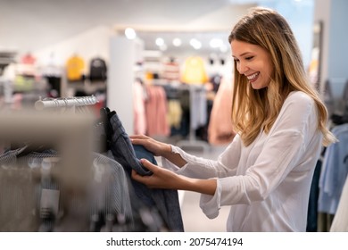 Happy Young Woman Buying New Clothes In Store. Sale Shopping Fashion And People Concept