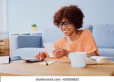 Happy young woman calculating figures with calculator at home
