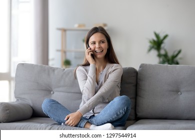 Happy Young Woman Caller Talking On The Phone At Home, Cheerful Teen Girl Enjoys Pleasant Mobile Conversation, Smiling Millennial Female Holding Cell Speaking Making Call By Telephone In Living Room