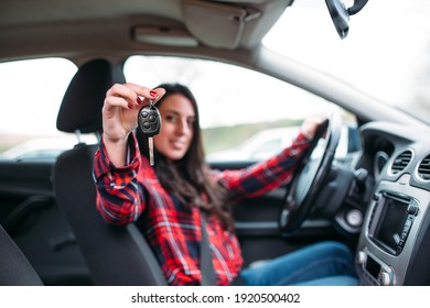 Happy young woman with car keys sits in her new car
