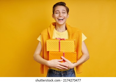 Happy Young Woman Carrying Gift Box While Standing Against Yellow Background