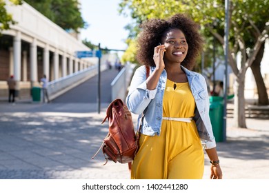 Happy Young Woman In Casual Walking While Talking Over Phone. Cheerful African American Girl With Curly Hair Using Smartphone. Black Curvy Woman Talking On Phone Outdoor.