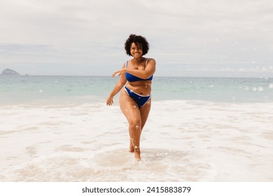 Happy young woman celebrating the spirit of summer on the beach, dancing joyfully in her bikini. Body confident, plus size woman having fun on a solo beach holiday. - Powered by Shutterstock