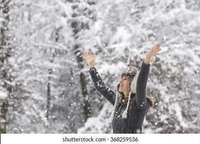 Happy young woman celebrating winter by raising her arms up in the air as she stands outside in beautiful nature in snowy weather.