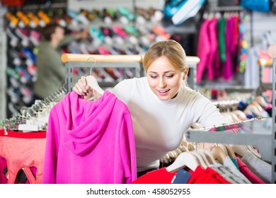 Happy Young Woman Choosing A Cardigan In The Sport Clothes Shop
