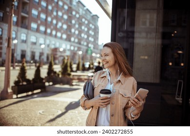 Happy young woman in city street drinking coffee and using smartphone - Powered by Shutterstock