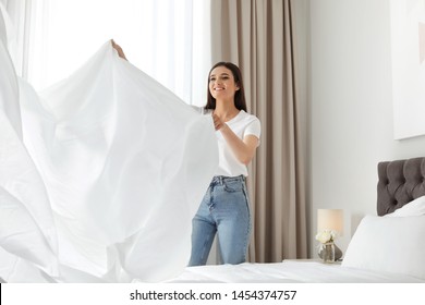 Happy young woman with clean bedsheet in room. Laundry day