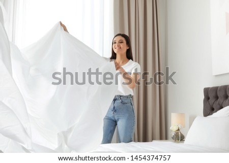 Happy young woman with clean bedsheet in room. Laundry day