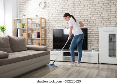 Happy Young Woman Cleaning The Hardwood Floor With Mop In Living Room