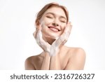 A happy young woman cleanses her skin with a gentle facial foam, the model applies the cleanser to her skin and smiles.