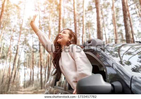 Happy young woman\
climbed out of a car window. Traveling by car in the forest.\
Country trip. Vacation by\
car