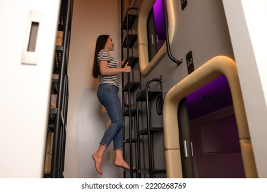 Happy Young Woman Climbing Up Ladder To Capsule In Pod Hostel, Low Angle View