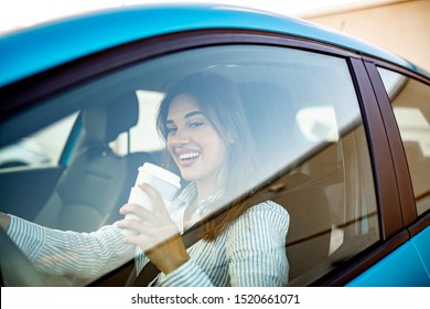 Happy young woman with coffee to go driving her car. Woman sipping a coffee while driving a car. Young woman drinking coffee while driving her car. Attractive brunette drives a ca