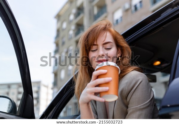 Happy young woman with coffee having a brake in her\
car. Side view of woman with coffee to go in hand. Young woman\
drinking coffee in her\
car