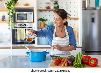 Happy Young Woman Cooking Tasting Dinner In A Pot Standing In Modern Kitchen At Home. Housewife Preparing Healthy Food Smiling . Household And Nutrition. Dieting Recipes Concept - Powered by Shutterstock